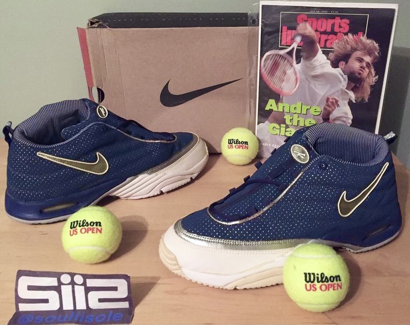 A pair of the Nike Air Assailant in the navy/silver/white colorway, along with the OG box, Agassi hat, Sports Illustrated magazine featuring Agassi and tennis balls. 