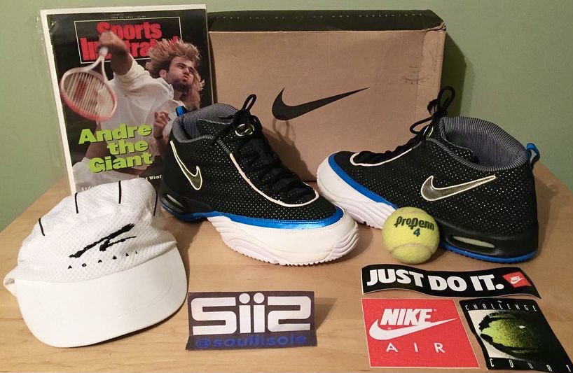 A pair of the Nike Air Assailant in the black/white/photo-blue colorway, along with the OG box, Agassi hat, Sports Illustrated magazine featuring Agassi and tennis balls. 